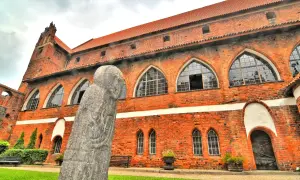 Kamienna postać strzeże murów zamku w Olsztynie. Czerwona cegła i łukowe okna tworzą majestatyczny widok.