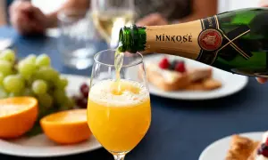 Une bouteille de Mimosé verse son contenu pétillant dans un verre rempli de jus d'orange. Un brunch festif se prépare.