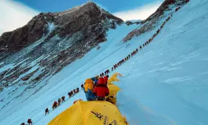 Eine lange Schlange von Bergsteigern kämpft sich den schneebedeckten Hang des Mount Everest hinauf. Die Frage, wie lange dauert es den Mount Everest zu besteigen, wird hier durch die schiere Anzahl der Menschen beantwortet.