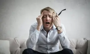 Man med händerna mot tinningarna, öppen mun, uttrycker ångest. Kanske dags för behandling av ångest.