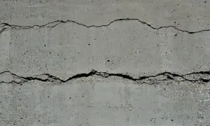 Zwei tiefe, unregelmäßige Risse durchziehen die graue Betonwand und zeugen von den Spuren der Zeit.