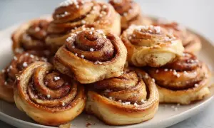 En hög med gyllene, glutenfria kanelbullar toppade med pärlsocker. Doftar ljuvligt av kanel och socker.