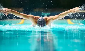 A swimmer powers through the water, arms extended in a strong butterfly stroke. This intense butterfly workout creates a splash.