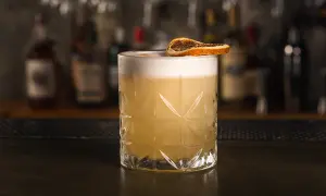 Klasyczny whisky sour przepis: orzeźwiający koktajl z pianką i plasterkiem suszonej pomarańczy na tle baru.