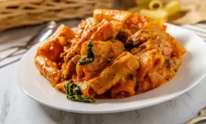 Makaron rigatoni w kremowym sosie pomidorowym ze szpinakiem i kawałkami mięsa.