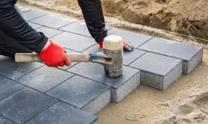 Pracownik w czerwonych rękawicach układa kostkę brukową, tworząc ciekawe aranżacje i wzory.
