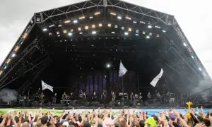 A massive crowd cheers at Glastonbury Festival, a testament to its huge capacity. Performers are on stage under a starry backdrop.