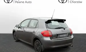 Szary Toyota Auris 2006 z przyciemnianymi szybami i spojlerem, zaparkowany na kostce brukowej.