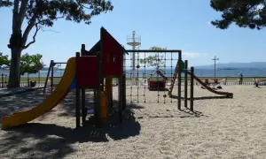 Un colorido parque infantil en la playa invita a jugar. Toboganes, redes y columpios esperan bajo el sol, con el mar de fondo.