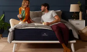 A couple enjoys coffee in bed. The DreamCloud hybrid mattress is on a white platform bed, answering the question: can you put a hybrid mattress on a box spring?