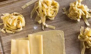 Frischer, selbstgemachter Pastateig, wie im original italienischen Rezept, liegt auf einem Holzbrett. Tagliatelle-Nester und Teigplatten warten auf ihre Zubereitung.