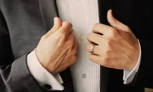 Manos ajustando su traje, mostrando un anillo de bodas. Un detalle elegante para saber donde poner anillos hombre.