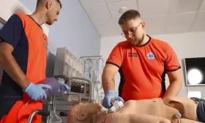 Uczestnicy kursu ratownika medycznego ćwiczą resuscytację na fantomie. Jeden z nich przygotowuje maskę oddechową, drugi uciska klatkę piersiową.
