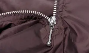 Zbliżenie na brązowy materiał z metalowym zamkiem. Podobnie jak w przypadku zamka w drzwiach wejściowych, ten mechanizm wymaga delikatnego pociągnięcia.