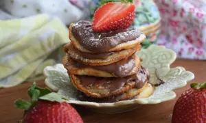 En hög med amerikanska pannkakor med nutella och färska jordgubbar. Pudrad med florsocker.