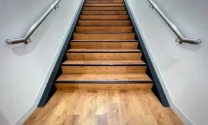 Moderne Treppe mit Holzoptik-Belag. Die Betonstufen sind professionell verkleidet, mit schwarzer Kante und Edelstahl-Handlauf.