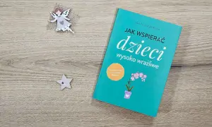 Książka "Jak wspierać dzieci wysoko wrażliwe" na drewnianym tle, obok aniołka i gwiazdki.