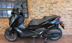 Czarny skuter Yamaha X-Max 125 na tle ceglanej ściany i okna.
