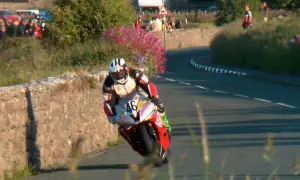 Motocyklista w kombinezonie i kasku ściga się na zakręcie drogi.