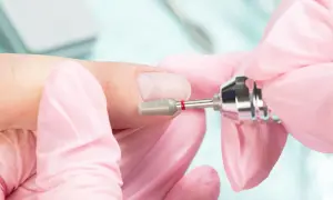 Dłonie w różowych rękawiczkach wykonują manicure frezarką. Przygotowanie paznokci do porodu, by były schludne i bezpieczne.