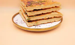 Stos kawałków omletu z odżywką białkową, udekorowany rozmarynem i fioletowym proszkiem, na talerzu.
