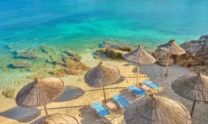 Piękna plaża w Albanii z turkusową wodą i słomianymi parasolami. Zastanawiasz się, ile się leci do Albanii?