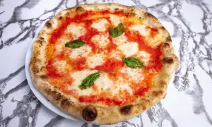 Domowa pizza neapolitańska z pomidorami, mozzarellą i bazylią na białym talerzu.
