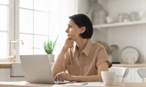 Kobieta przy laptopie, zamyślona, szuka informacji o kodzie tytułu ubezpieczenia.