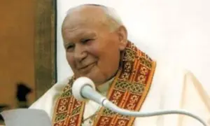 Jan Paweł II z uśmiechem przemawia do wiernych, trzymając w ręku tekst. Jego barki zdobi ozdobna stuła.