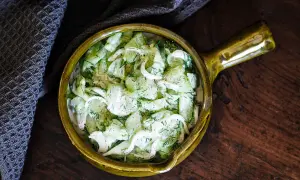 Salade de concombre à la crème, garnie d'aneth frais, servie dans un bol en céramique jaune sur une table en bois rustique.