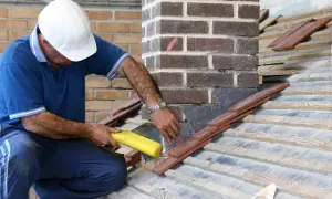 Un couvreur assure l'étanchéité de la cheminée sur la toiture avec du plomb et des tuiles.