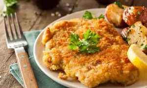 En gyllene schnitzel med dubbel panering, serverad med rostade potatisar och citronklyfta.