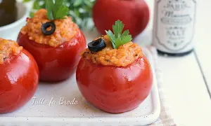 Pomodori ripieni di riso, guarniti con olive nere e prezzemolo, su un piatto bianco.