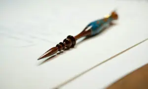 Eleganckie pióro do kaligrafii, ozdobione niebieskimi i złotymi detalami, leży na papierze. Może posłużyć do stworzenia dzieła sztuki, zgodnie z art. 63 kp.