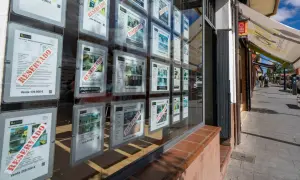 Escaparate de inmobiliaria con anuncios de venta de casas, muchos marcados como "RESERVADO". Se vislumbra una casa señorial en uno de los carteles.