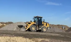 Chargeuse jaune en action pour décaissement de terrain, entourée de tas de gravats et de terre sous un ciel bleu clair.