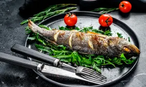 Un bar au four, doré et savoureux, servi sur un lit de roquette avec des tomates cerises et des herbes. Un plat simple et élégant.