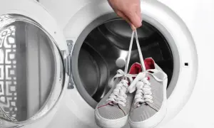 Ręka trzyma sznurowane trampki nad otwartą pralką. Dowiedz się, jak prać buty w pralce, aby były jak nowe.