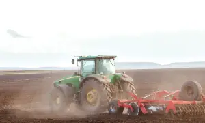 Zielony traktor orze pole. To obraz przyszłości, gdzie przekazanie gospodarstwa rolnego idzie w parze z opieką nad rodzicami, zapewniając stabilność i ciągłość.