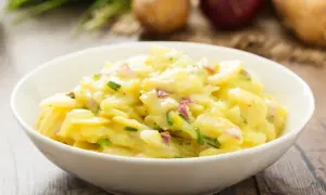 Omas Kartoffelsalat in einer Schüssel, mit Zwiebeln und Schnittlauch, auf einem Holztisch.