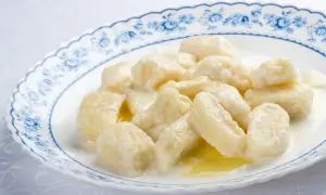 Pyszne kopytka z serem, polane śmietaną i masłem, na talerzu z niebieskimi kwiatami.