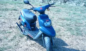 Niebieski skuter Yamaha MBK z czerwonymi akcentami stoi na trawiastym podwórku.