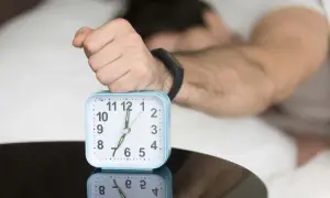 A hand rests on an alarm clock showing 7:00, reflecting the question: is four hours of sleep enough?