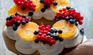 Torta pavlova a forma di corona, decorata con fette d'arancia, ribes rossi e mirtilli.