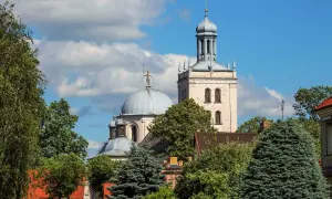 Majestatyczna fara w Grodzisku Wlkp. z kopułą i wieżą, otoczona zielenią drzew.