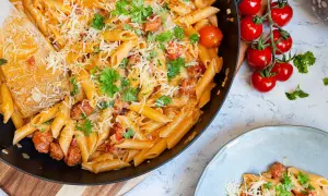 En stor panna med krämig pasta med chorizo, toppad med riven ost och färsk persilja. Bredvid syns en tallrik med samma läckra pasta.