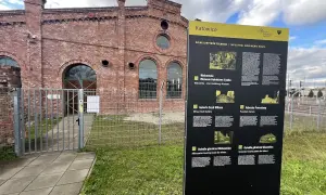 Tablica informacyjna Szlaku Zabytków Techniki w Katowicach, obok ceglanej budowli dawnej huty.