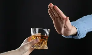 Ręka odrzuca szklankę z alkoholem. Czy dzień przed wyrwaniem zęba można pić alkohol? Lepiej unikać.