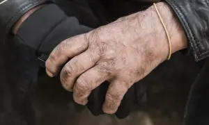 Manos secas y curtidas, con una goma elástica en la muñeca, sujetan un guante negro.