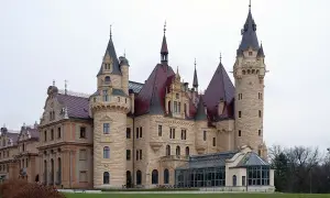 Kamienny zamek z czerwonymi dachami i wieżami, przypominający najstarsze zamki w Polsce.